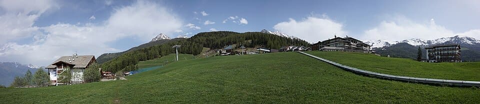 A wide landscape panorama of Pila ski resort in the Aosta Valley, showing the snow-covered slopes and mountain backdrop under a blue sky