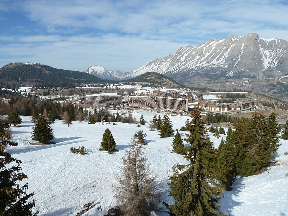 A wide landscape view of the SuperDévoluy resort building set against the snow-covered alpine peaks